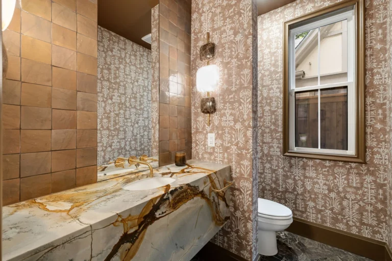Luxury guest bathroom with patterned wallpaper, brass fixtures, and a dramatic stone vanity